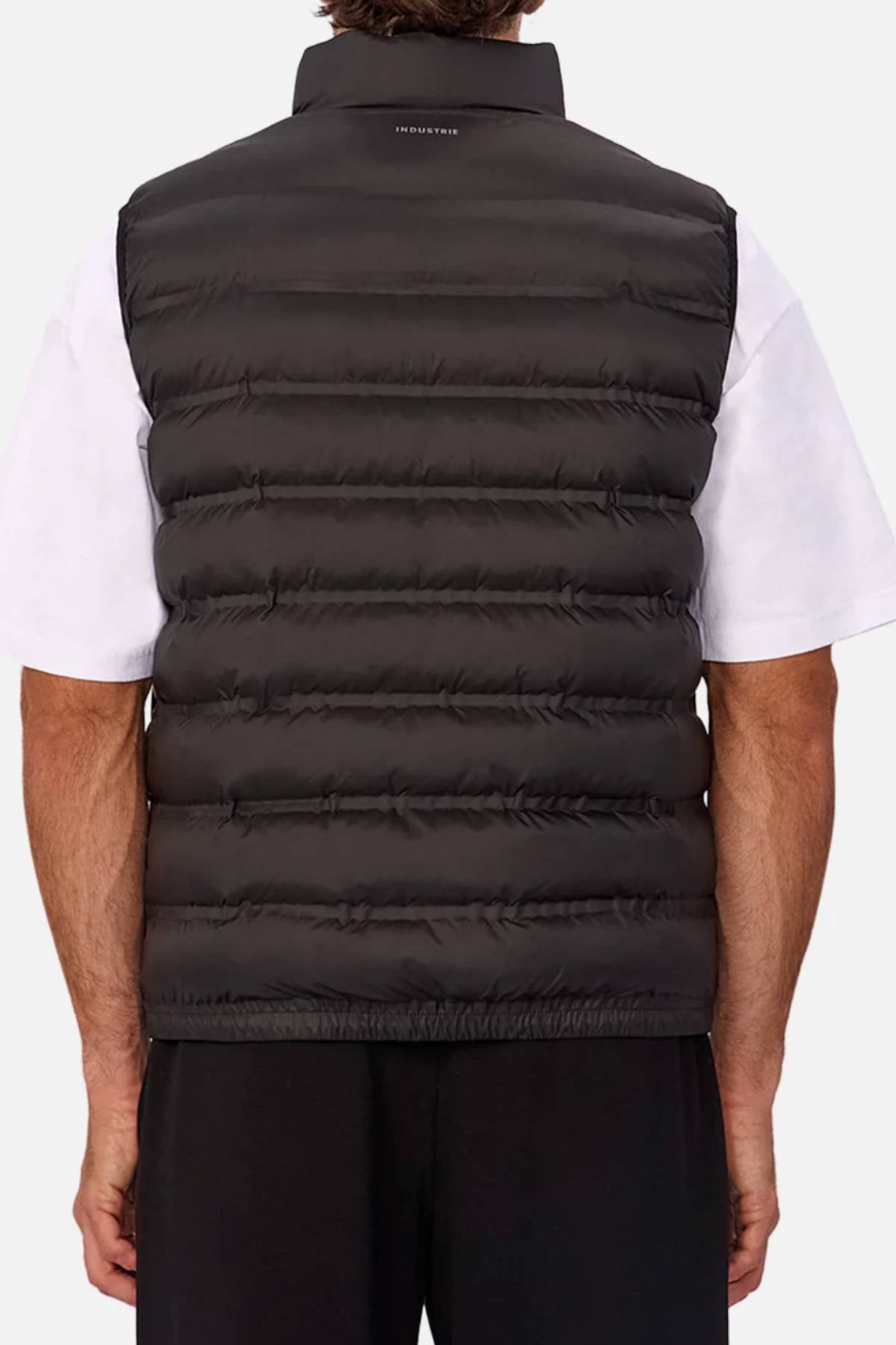 A person wearing the Industrie The Kyoto Puffer Vest in black over a white short-sleeve shirt and black pants, shown from the back against a plain light background.