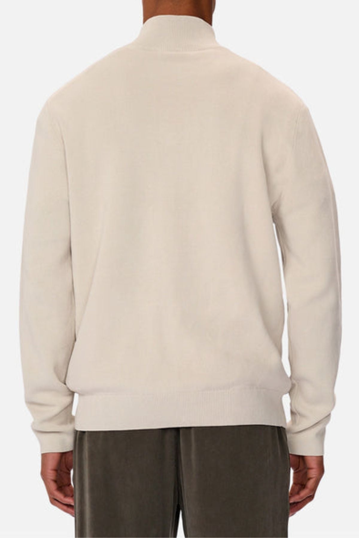 A person is shown from the back, standing against a plain white background, wearing the Industrie The Lakewood Zip Neck—a long-sleeved, light beige cotton jumper with rib knit cuffs—and dark pants.