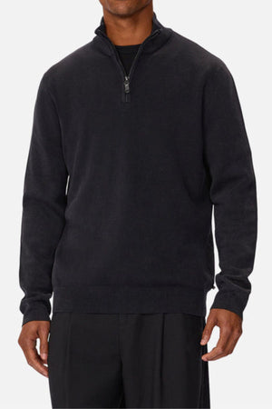 A man wearing the Industrie The Lakewood Zip Neck, a black regular fit cotton jumper, over a black shirt and pants, stands against a plain white background.