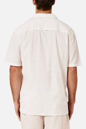 A man is shown from the back wearing the Industrie The Magna Short Sleeve Shirt, a short-sleeved white shirt with breathable, textured fabric and an oversized fit, paired with light-colored shorts against a plain white background.