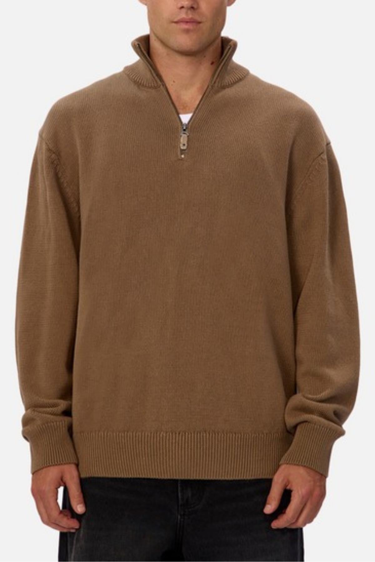 Wearing the Industrie The Maine Zip Neck Knit—a brown, heavyweight cotton sweater with a high collar and ribbed details—a person stands against a plain white background, paired with regular-fit dark pants.