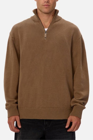Wearing the Industrie The Maine Zip Neck Knit—a brown, heavyweight cotton sweater with a high collar and ribbed details—a person stands against a plain white background, paired with regular-fit dark pants.