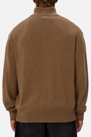 A person is shown from the back wearing the Industrie The Maine Zip Neck Knit, a light brown ribbed heavyweight cotton sweater with a high collar and regular fit, paired with dark pants against a plain light background.