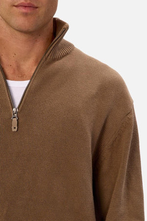 A man wears the Industrie The Maine Zip Neck Knit, a regular fit, heavyweight brown cotton quarter-zip sweater, layered over a white shirt. He is shown from the shoulders up against a plain background.