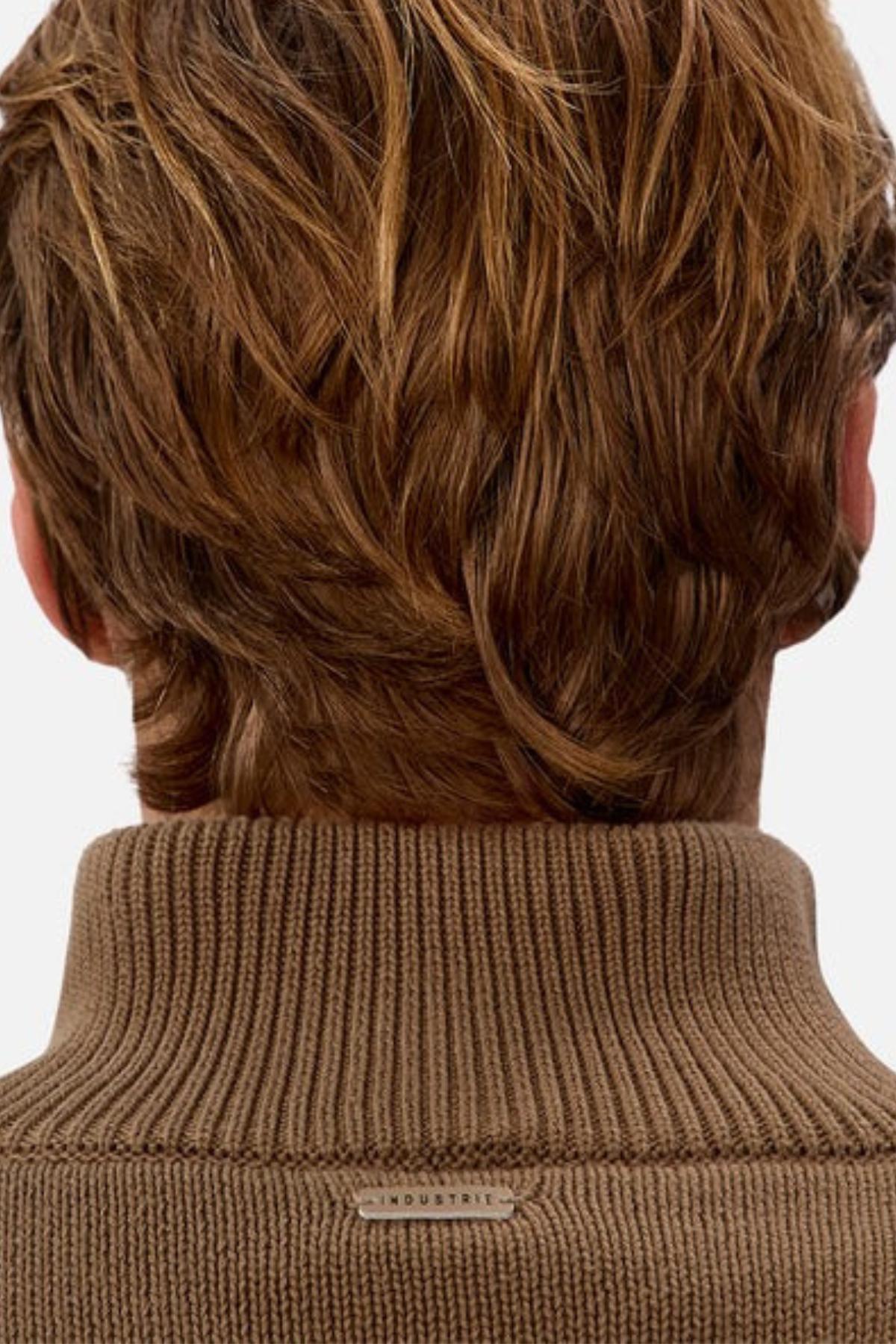 A close-up of the back of a person's head with light brown, wavy hair. They are wearing the Industrie The Maine Zip Neck Knit, a ribbed brown turtleneck with a small "INDUSTRIE" tag at the neck.