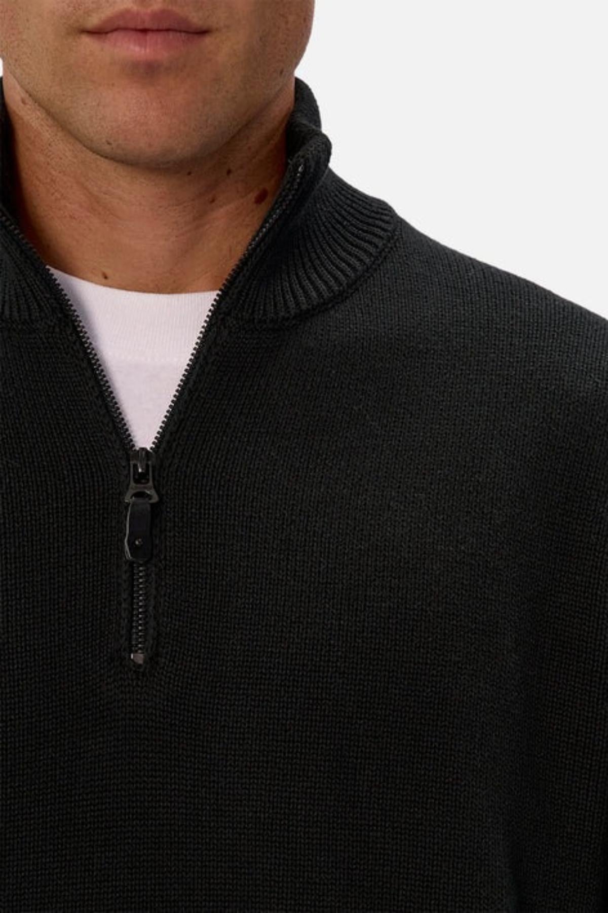 Close-up of a person in the Industrie The Maine Zip Neck Knit, a regular fit black cotton quarter-zip sweater worn over a white t-shirt. The zipper is partly open, showing just the lower face and upper torso.