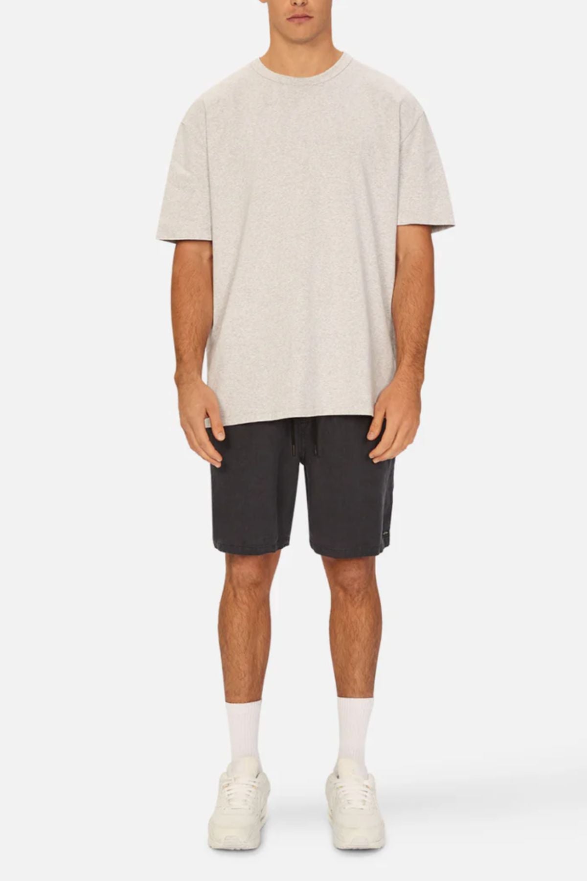 A man stands facing forward in a light gray t-shirt and Industrie The Marina Linen Short in black, featuring a drawcord waist. He pairs them with white crew socks and white sneakers. His arms rest at his sides against a plain white background.