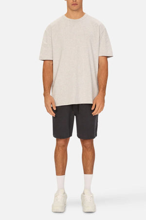 A man stands facing forward in a light gray t-shirt and Industrie The Marina Linen Short in black, featuring a drawcord waist. He pairs them with white crew socks and white sneakers. His arms rest at his sides against a plain white background.