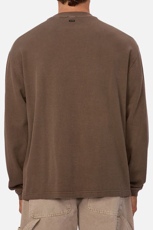 A person shown from the back wears the loose-fitting Industrie The Marlon Long Sleeve Tee in brown with light cargo shorts, set against a plain white background. This versatile tee is made from 100% cotton.