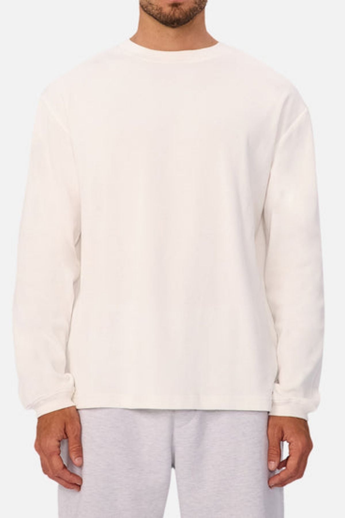 A man in an Industrie The Marlon Long Sleeve Tee, crafted from 100% cotton, and light gray sweatpants stands against a neutral background with his face partially out of frame.