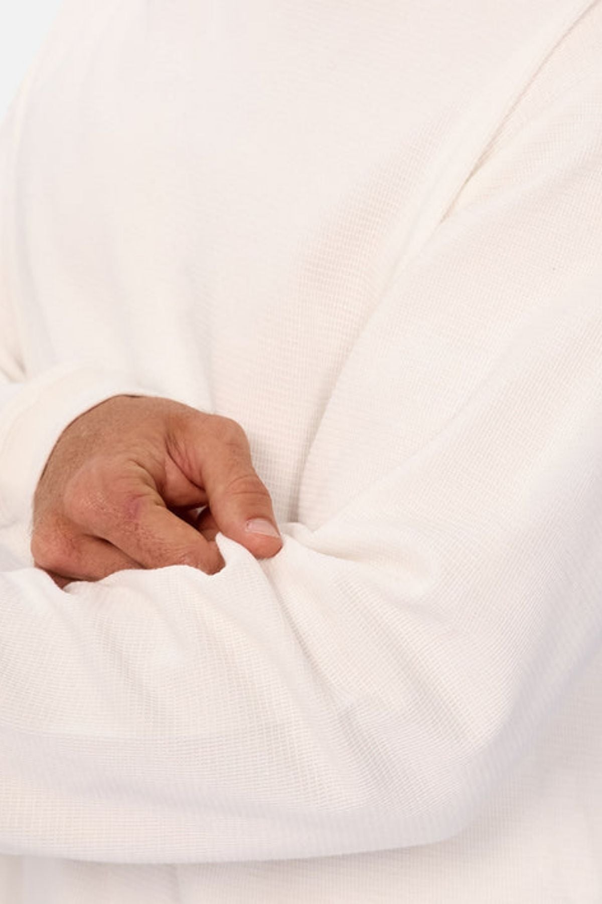 A person is shown from the shoulders down wearing the Industrie The Marlon Long Sleeve Tee in white, 100% cotton, with one arm crossed and their hand gently holding the opposite sleeve near the elbow.