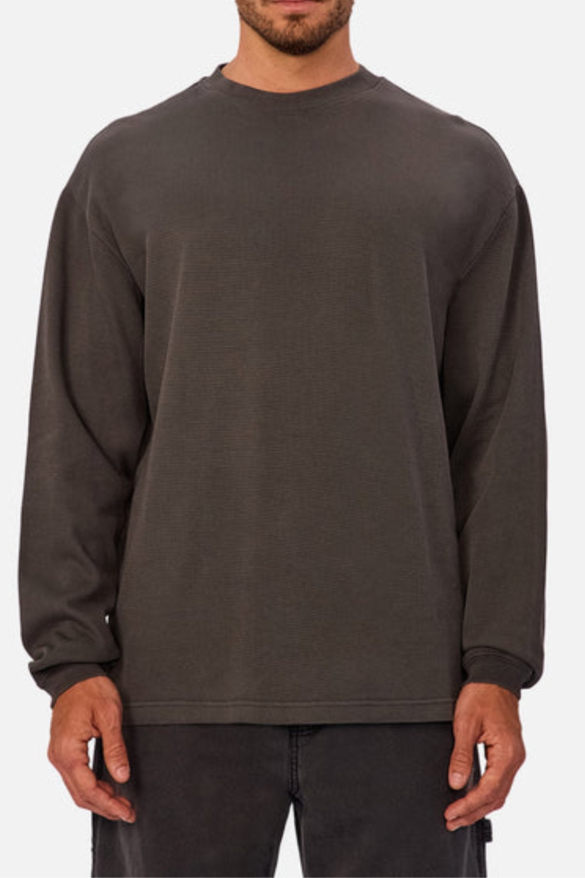 A man wears the Industrie The Marlon Long Sleeve Tee, made from 100% cotton with a refined textured finish, paired with dark pants and standing relaxed against a plain light background.