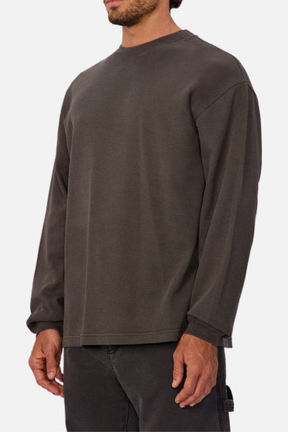 A person, face partially out of frame, wears a loose-fitting dark gray Industrie The Marlon Long Sleeve Tee made from 100% cotton textured fabric with matching pants, standing against a plain white background.