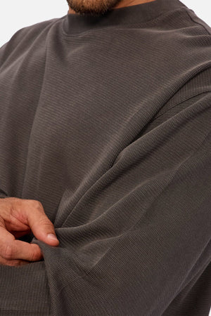 Close-up of a person in the Industrie The Marlon Long Sleeve Tee, made from 100% cotton with refined textured fabric, gently tugging at their sleeve near the elbow. Only their lower face and body are shown.
