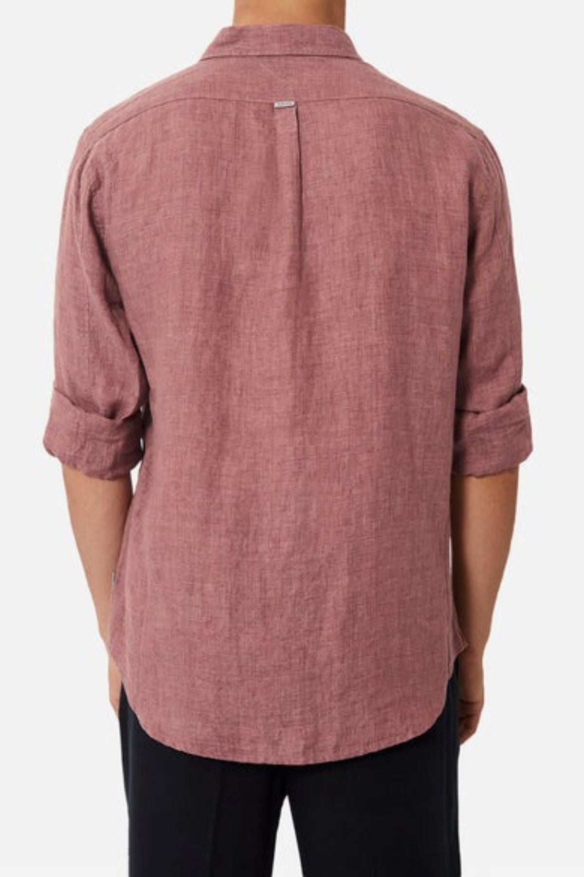A person stands with their back to the camera, showcasing Industrie The Midland Shirt—a long-sleeve, button-up shirt in a soft reddish hue. The sleeves are casually rolled up, complemented by their dark pants, exuding the casual elegance typical of INDUSTRIE branding.
