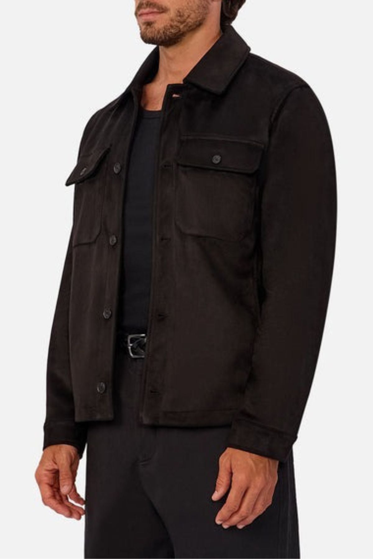 A man wears the Industrie The Monaco Jacket—a versatile black button-up with chest flap pockets and lined torso and sleeves—over a black shirt and pants, standing against a plain light background.