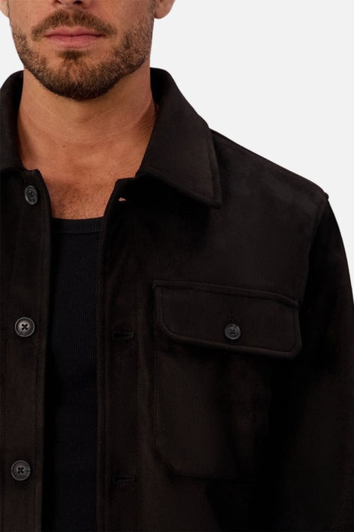 A man with a short beard wears the Industrie The Monaco Jacket—a versatile black jacket with a front pocket, black buttons, and lined torso and sleeves for comfort—over a black shirt, shown chest up against a plain light backdrop.