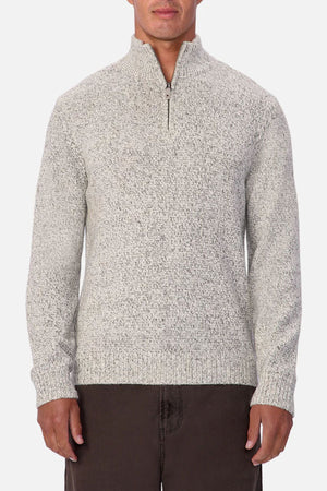 A person wears the Industrie The Montauk Knit—a light gray, marled zip-neck pullover sweater with a textured finish—paired with dark pants, standing against a plain white background.