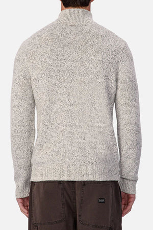 A person is seen from behind wearing the Industrie The Montauk Knit in light gray with a zip neck and marled knit texture, paired with dark brown pants against a plain white background.