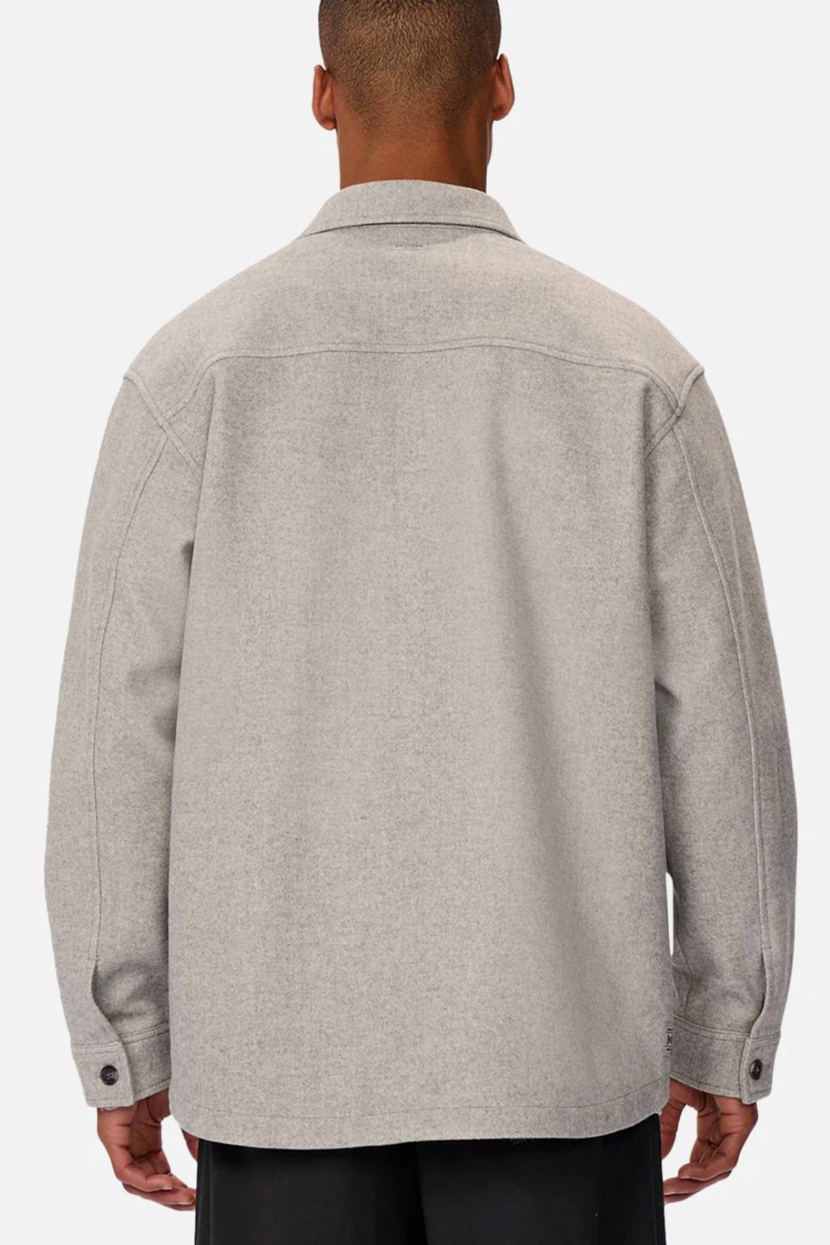 A person is shown from behind wearing the Industrie The New Coleman Jacket in light gray with a classic collar, relaxed fit, and long sleeves with buttoned cuffs, paired with black pants.