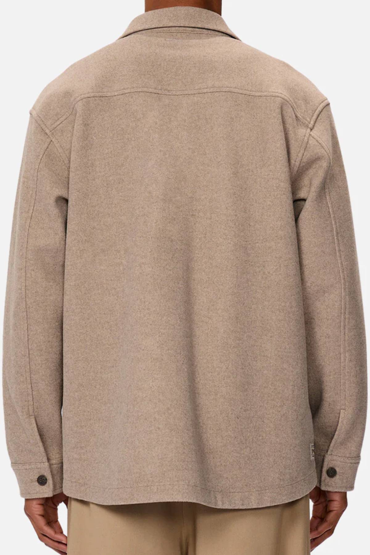 A person is seen from the back wearing the Industrie The New Coleman Jacket, a beige wool jacket with long sleeves, twin chest pockets, classic collar, buttoned cuffs, and a relaxed fit, paired with light-colored trousers.