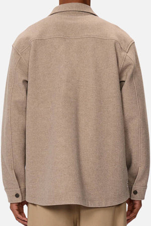 A person is seen from the back wearing the Industrie The New Coleman Jacket, a beige wool jacket with long sleeves, twin chest pockets, classic collar, buttoned cuffs, and a relaxed fit, paired with light-colored trousers.