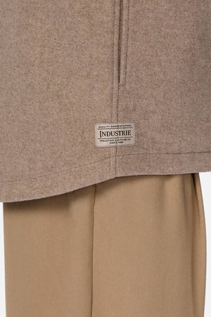 A close-up of the Industrie The New Coleman Jacket with a classic collar, visible seam, and "Industrie" tag, styled over light brown pants.