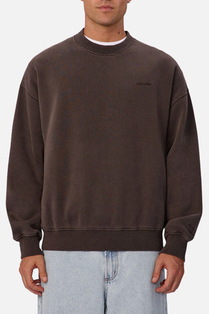Someone wears the loose-fitting Industrie The New Del Sur Sweatshirt in dark brown with subtle chest branding and light blue jeans, standing against a plain white background.