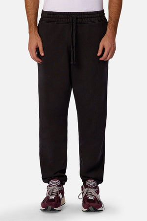 A person wearing Industrie The New Del Sur Trackpant in black, paired with a white shirt and maroon sneakers, stands against a plain light background. Only the lower half of the body is visible.