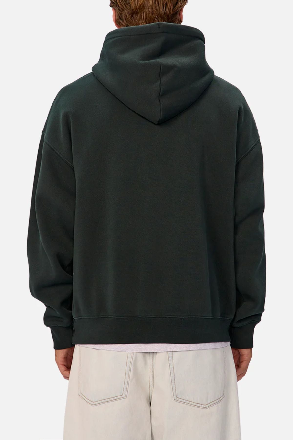 A person is seen from behind wearing the Industrie The New Del Sur Washed Hoodie in dark green with the hood down, paired with light pants. The background is plain and light-colored.