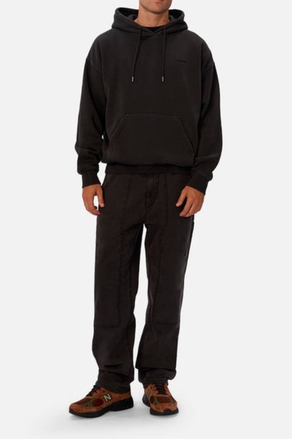 A person in an Industrie The New Del Sur Washed Hoodie with an oversized fit, black pants, and brown New Balance sneakers stands against a plain white background.