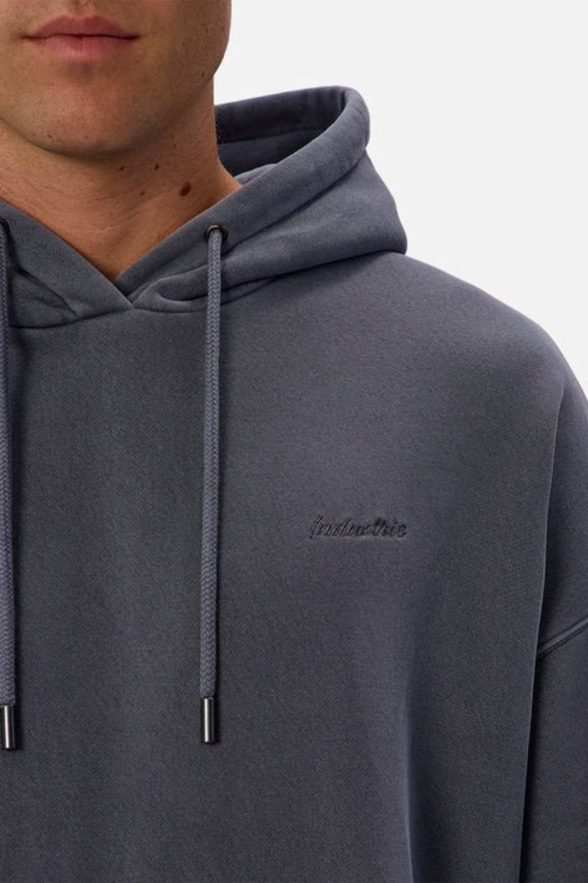 A person wearing the Industrie The New Del Sur Washed Hoodie, featuring an oversized fit and subtle embroidered text on the left chest, is shown from the shoulders up against a plain background.
