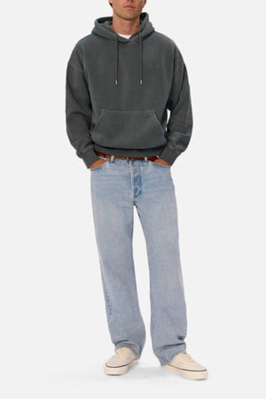 A person stands against a plain white background wearing the Industrie The New Del Sur Washed Hoodie in dark gray, paired with light blue jeans and white sneakers, with their hands in their pockets.