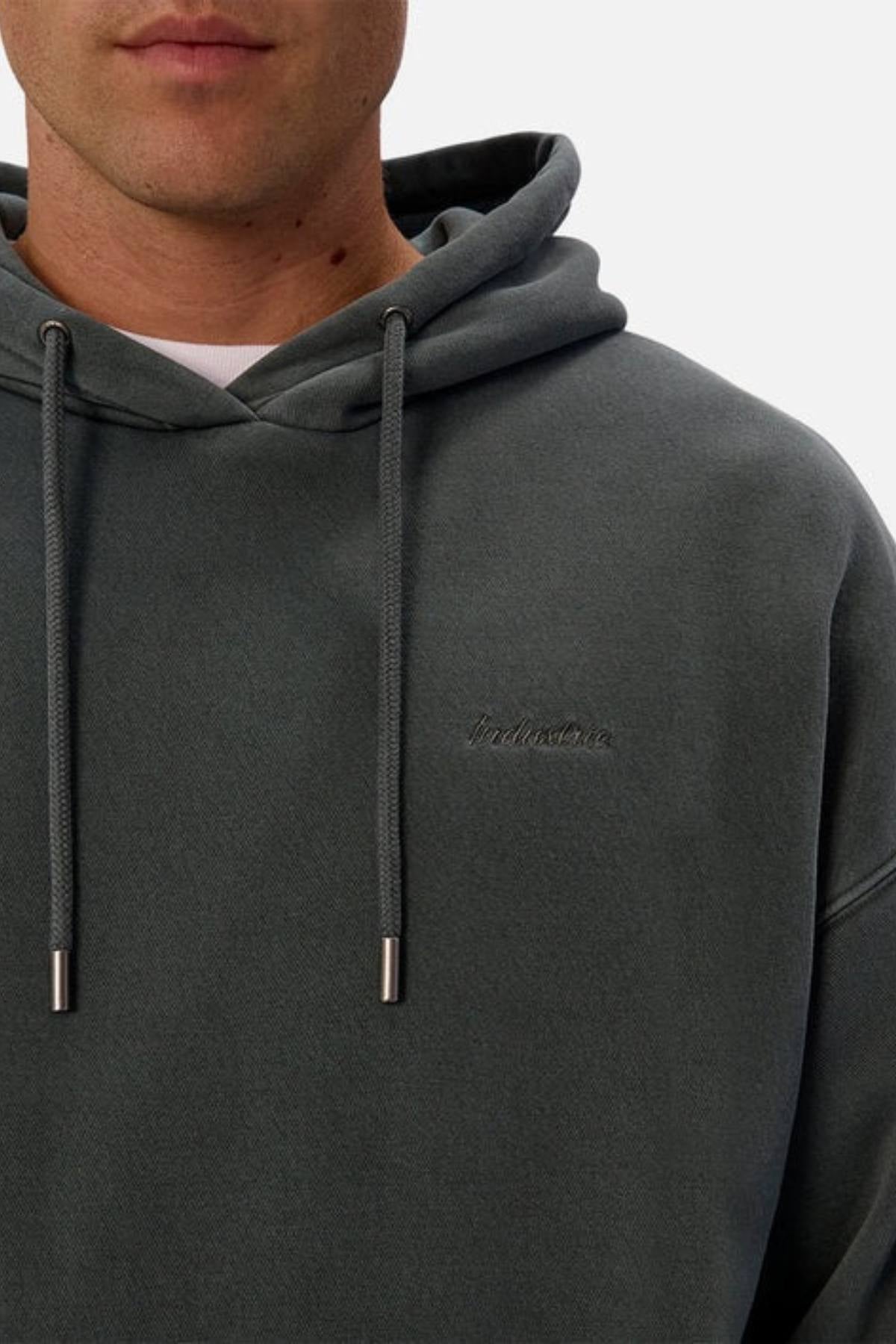 Someone wearing the Industrie The New Del Sur Washed Hoodie in dark grey, featuring drawstrings and subtle chest embroidery, shown from the shoulders up against a plain background.