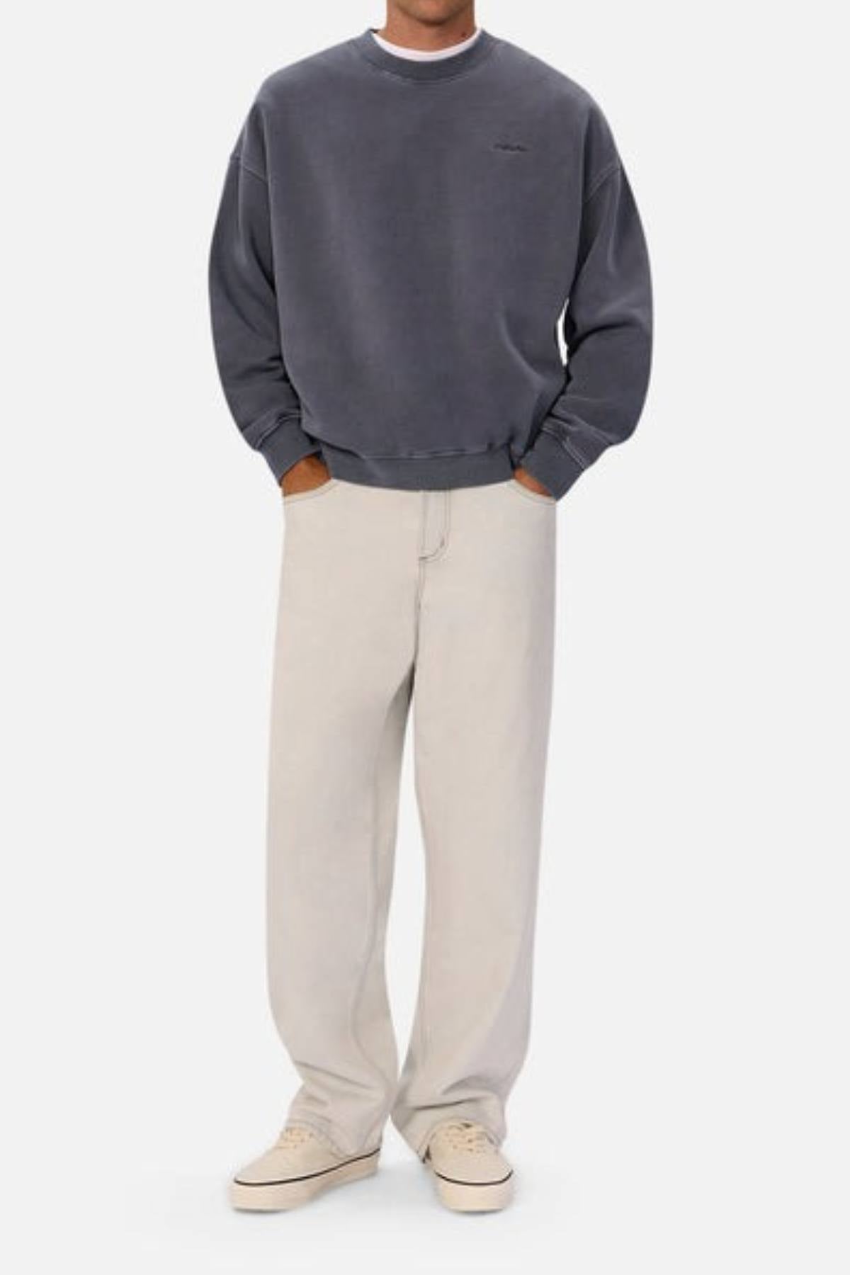 Wearing an oversized gray Industrie The New Del Sur Washed Sweat, off-white wide-leg pants, and beige sneakers, a person stands with hands in pockets against a plain light background.