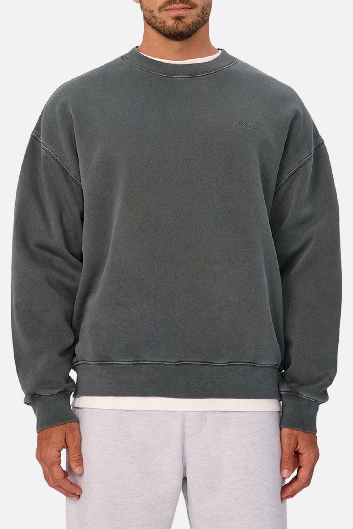 A man wears an oversized, faded dark gray Industrie The New Del Sur Washed Sweat over a white tee and light gray shorts against a plain white background, with the Industrie logo visible as his face is partially out of frame.