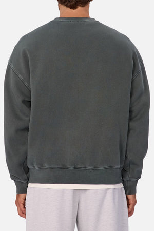 A person is seen from the back wearing an oversized Industrie The New Del Sur Washed Sweat in faded dark gray over a white T-shirt and light gray shorts. The focus is on the clothing, with a subtle Industrie logo and only part of the head and legs visible.
