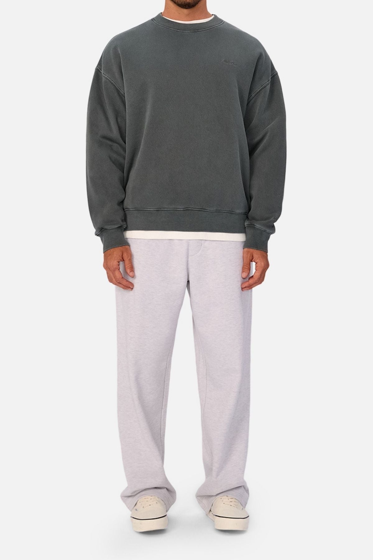 A man models the oversized Industrie The New Del Sur Washed Sweat in dark grey, paired with loose light grey sweatpants and off-white sneakers against a plain backdrop. His face remains out of view.