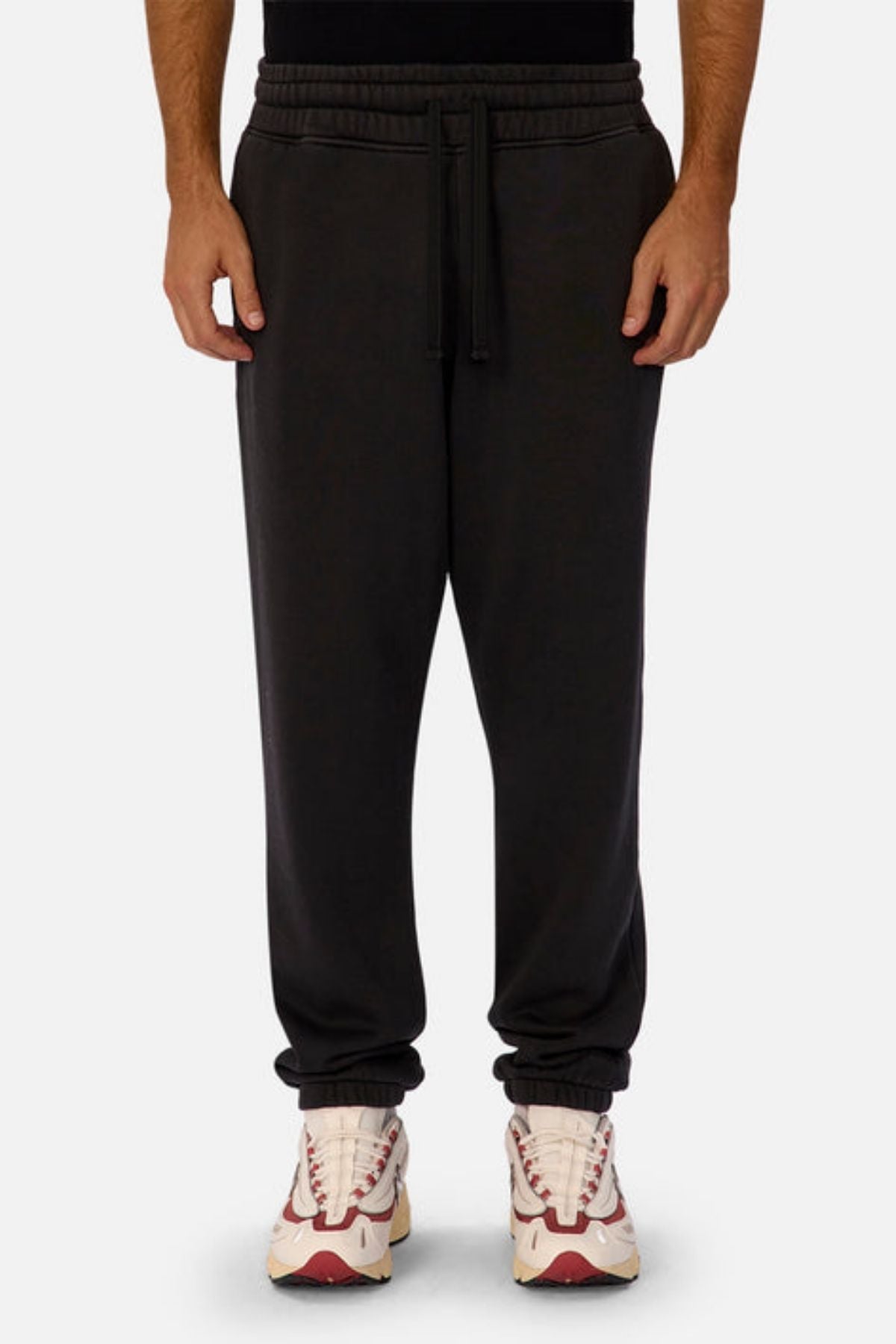 Wearing Industrie The New Del Sur Washed Trackpant with a drawstring waist and elastic cuffs, and white sneakers with red accents, a person stands against a plain light background.