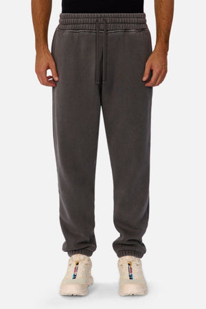 A person is shown standing against a plain white background, wearing Industrie The New Del Sur Washed Trackpant in dark gray with an oversized fit, elastic waistband, and drawstring, paired with white sneakers.