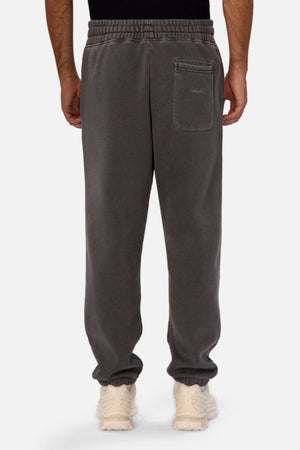 A person wearing Industrie The New Del Sur Washed Trackpant, featuring gray fabric, elastic waistband and cuffs, a small back right pocket, and a relaxed fit. Cream sneakers complete the laid-back style, as seen from the back.