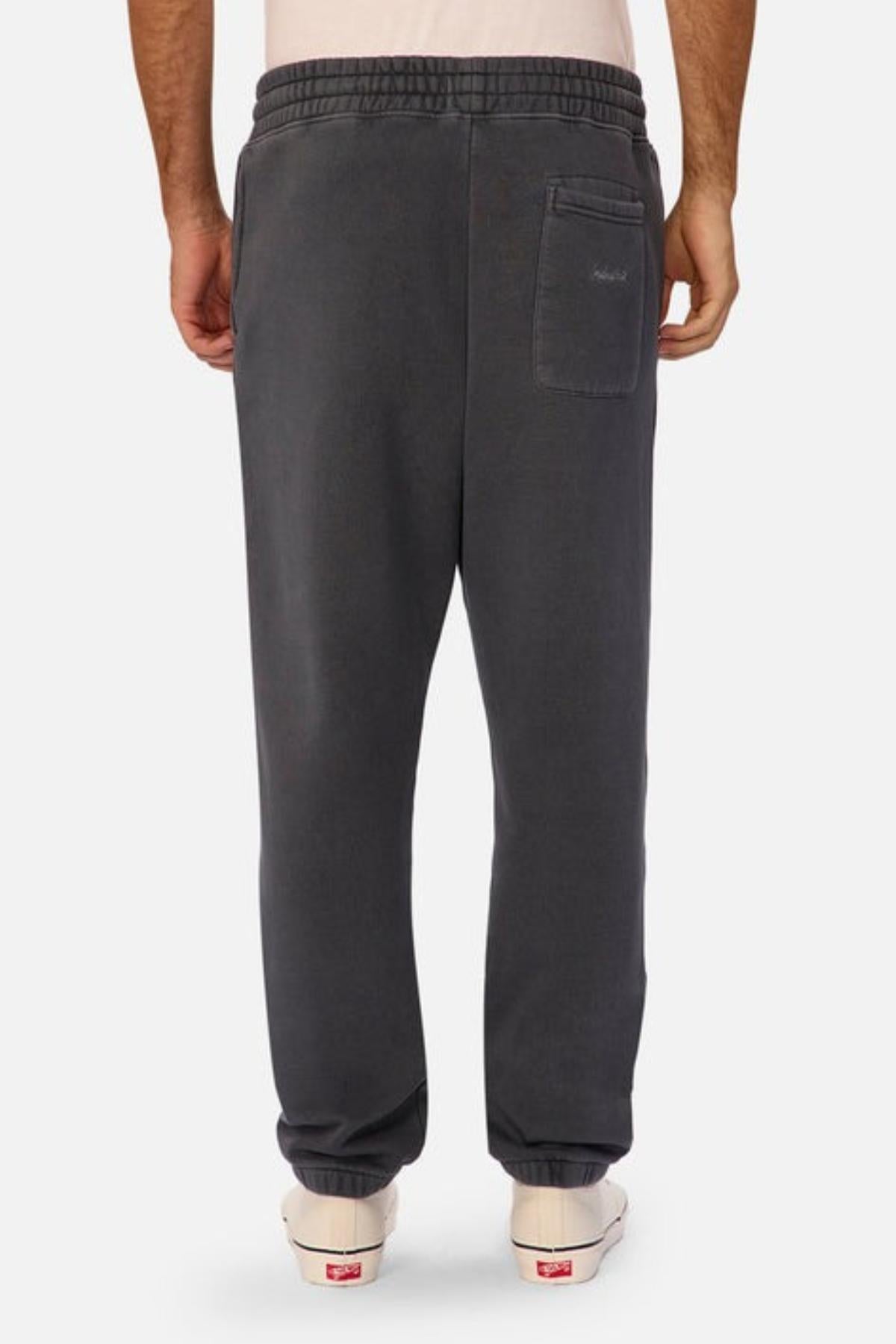 A person is seen from the back wearing Industrie The New Del Sur Washed Trackpant in dark gray with an oversized fit, single back pocket, elastic waistband and cuffs, paired with white sneakers against a plain white background.