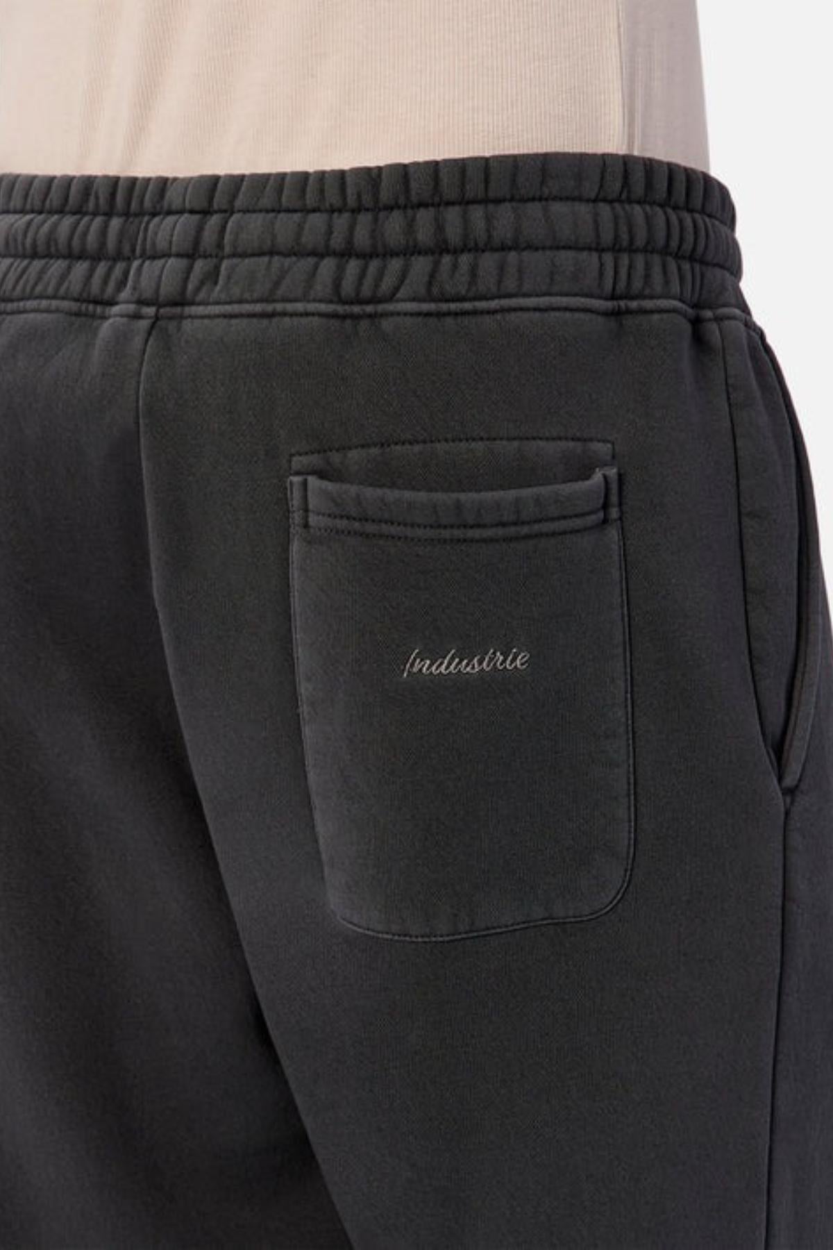 Close-up of a person wearing the Industrie The New Del Sur Washed Trackpant, featuring an elastic waistband, back pocket with "Industrie" embroidery, and an oversized fit. Paired with a light shirt for easy style.