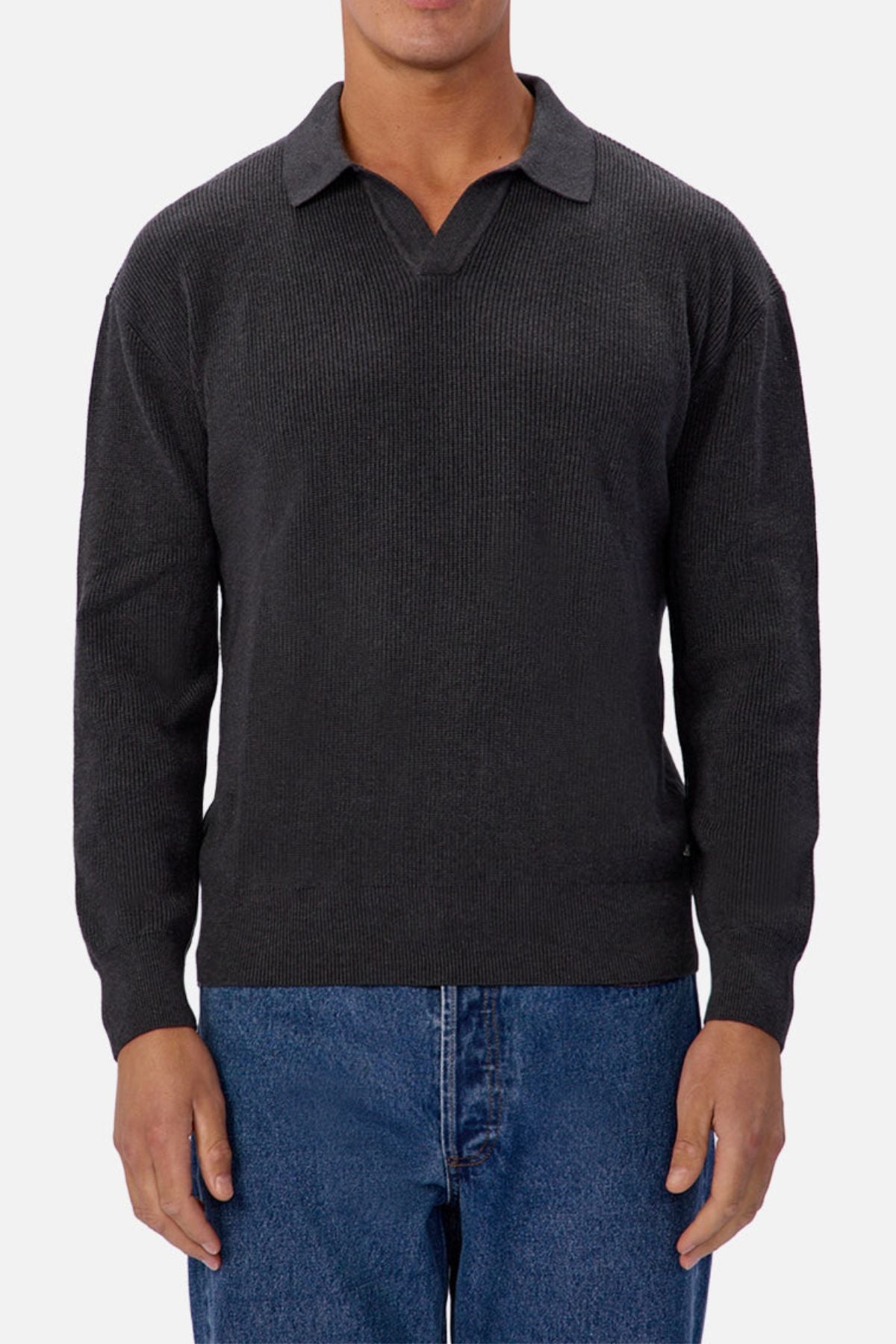 A man wears the Industrie The New England Polo Knit, a dark gray sweater with a collar and V-notch neckline, paired with blue jeans, standing against a plain white background.