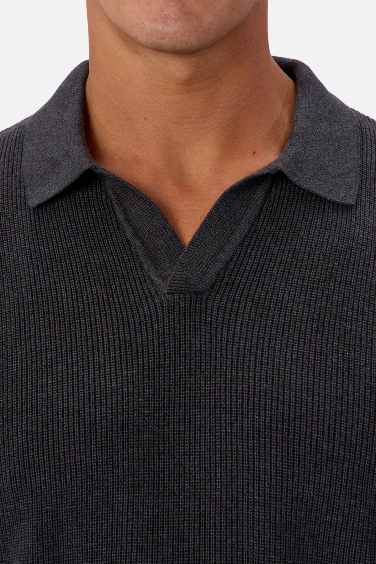 A close-up of a person wearing the Industrie The New England Polo Knit, featuring a dark color and V-shaped neckline. Only the lower face, neck, and upper chest are visible in the cropped image.