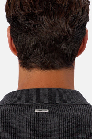 A close-up of the back of a person’s head shows short, wavy brown hair and a dark Industrie The New England Polo Knit sweater with a small metallic label on the collar.