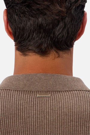A close-up of the back of a person’s neck and head with short dark hair, wearing Industrie The New England Polo Knit—a ribbed brown 100% cotton polo featuring a small rectangular metallic tag below the collar.