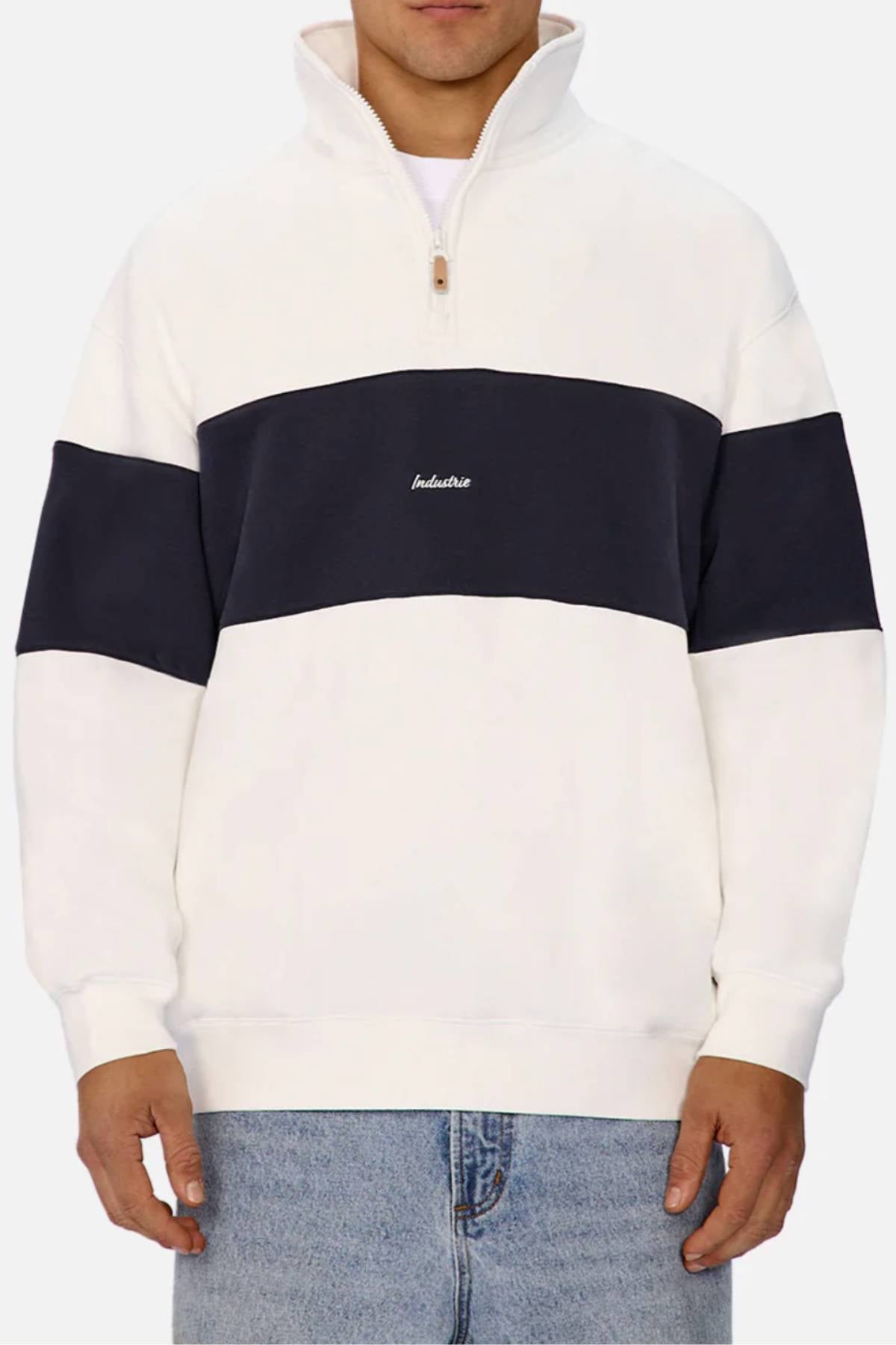 A person wears the Industrie The New Luton Track Top, a white men's track top with a wide black stripe, modern panelled design, “Industrie” embroidered on the chest, paired with light blue jeans.