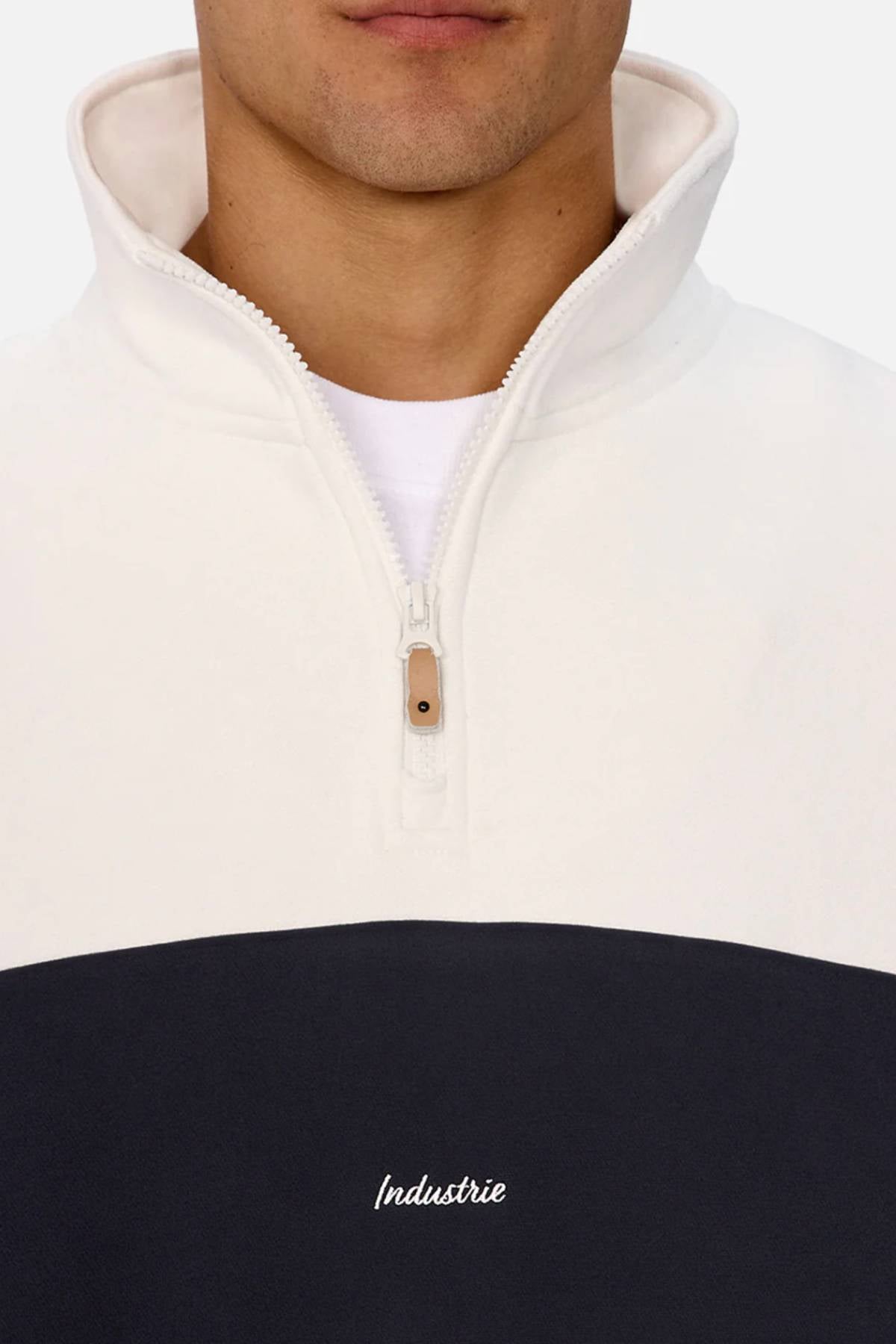 A person wears the Industrie The New Luton Track Top, a men's jacket with a white and navy panelled design and "Industrie" embroidery, partially zipped over a white shirt.