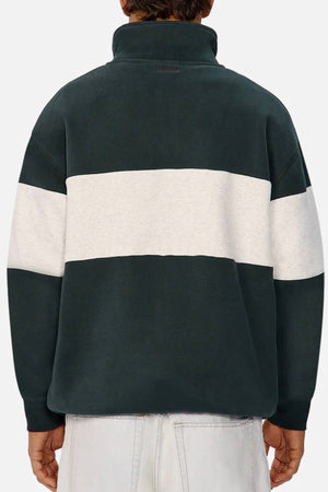 A person is seen from the back wearing Industrie The New Luton Track Top in relaxed fit dark green with a thick white stripe and high collar, paired with light-wash jeans for a casual look.